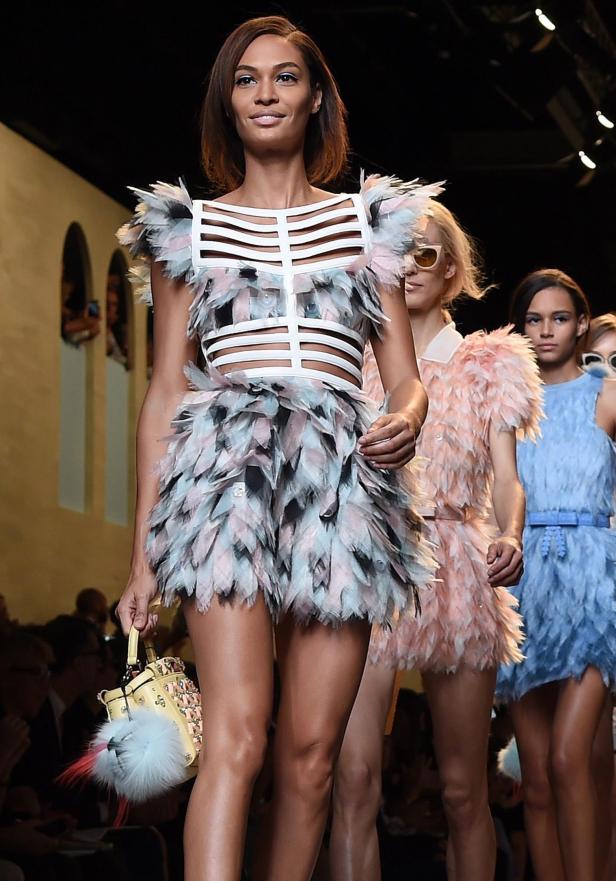 Eine Frau in einem Federkleid mit passender Handtasche auf dem Laufsteg.