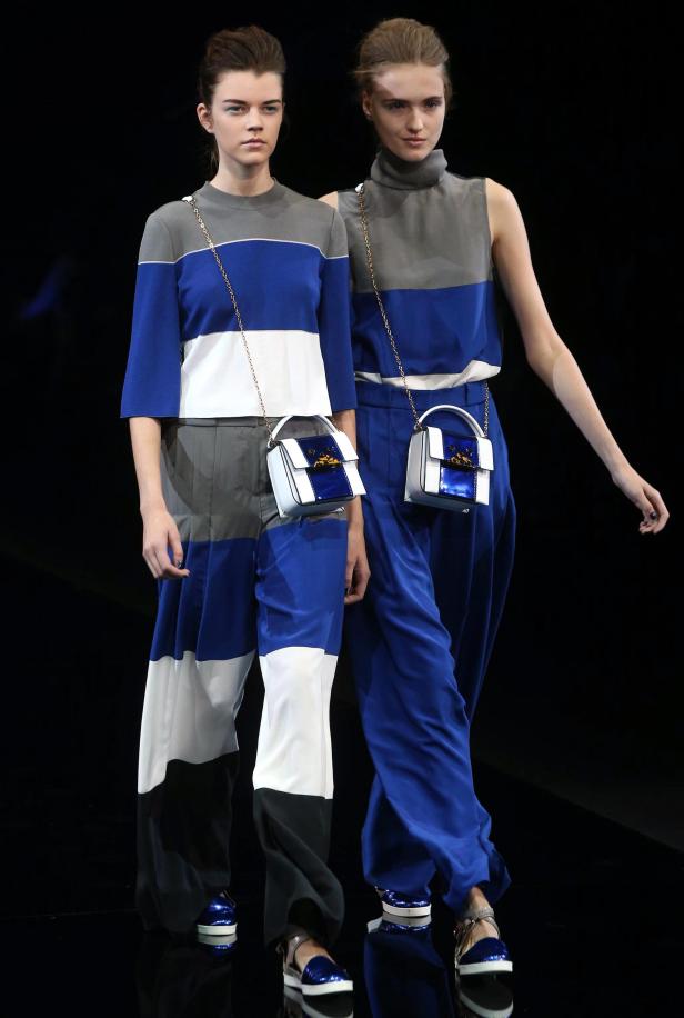 Zwei Models präsentieren farblich abgestimmte Outfits und Handtaschen auf dem Laufsteg.