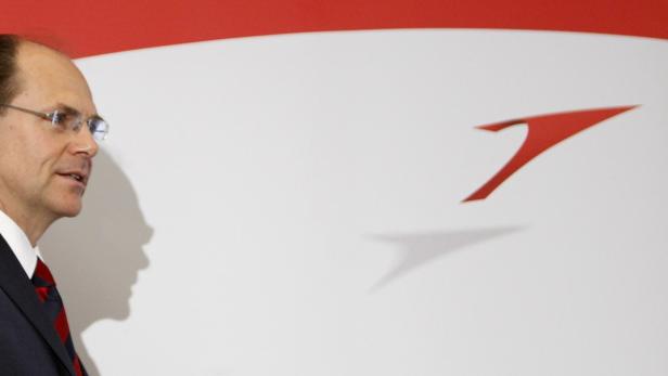 Ein Mann mit Brille steht vor einem roten Logo auf einer weißen Wand.