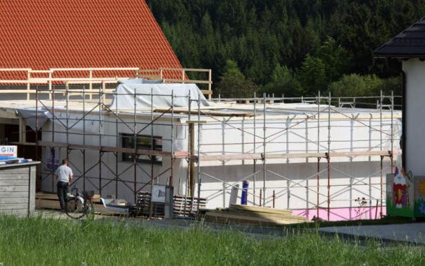 Ein Rohbau mit Gerüst steht vor einem bewaldeten Hügel.