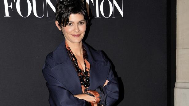 Audrey Tautou posiert mit verschränkten Armen vor einem schwarzen Hintergrund.