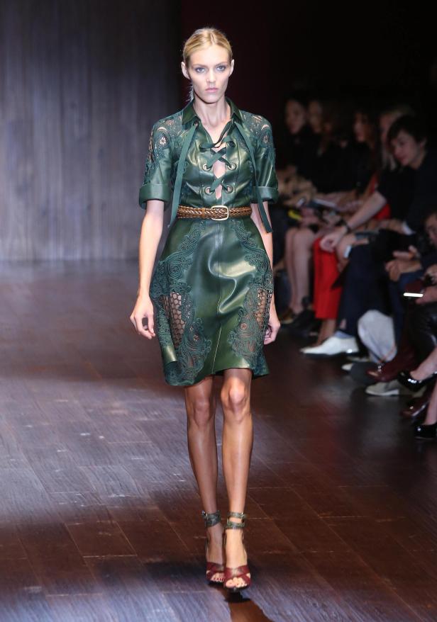 Eine Frau präsentiert ein grünes Lederkleid mit Spitze auf einem Laufsteg.