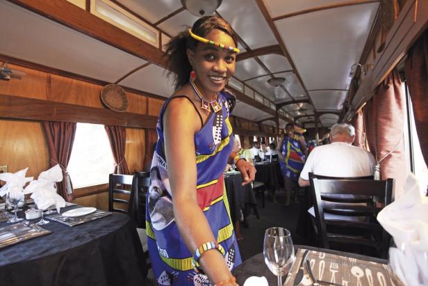 Eine lächelnde Frau in traditioneller Kleidung serviert in einem Speisewagen eines Zuges.