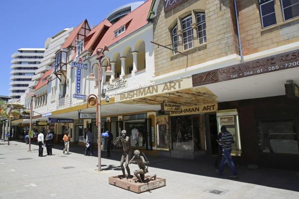 Eine belebte Straße in Windhoek mit Geschäften und einer Statue von Buschmännern.