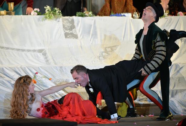 Eine Theaterszene mit einer sterbenden Frau und zwei Männern in Kostümen.