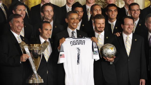 Barack Obama hält ein Trikot mit seinem Namen und der Nummer 1, umgeben von Fußballspielern.