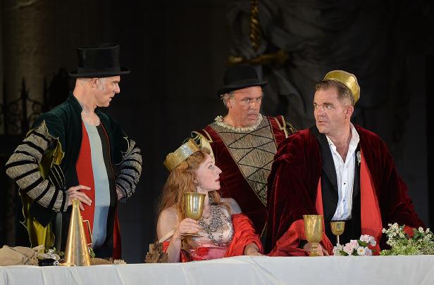Szene aus einem Theaterstück mit Schauspielern in historischen Kostümen an einer Tafel.