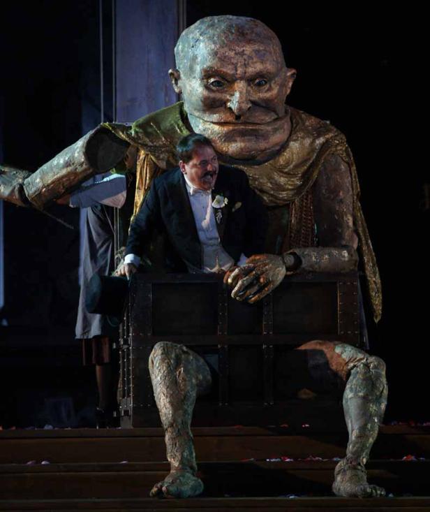 Ein Mann im Smoking steht in einer Kiste, die Teil einer riesigen Statue ist.