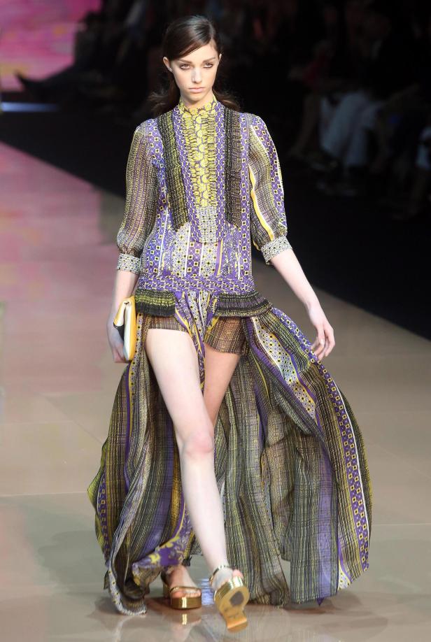 Ein Model präsentiert ein gemustertes Kleid mit hohem Schlitz auf dem Laufsteg.