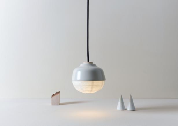 Eine graue Hängelampe beleuchtet eine minimalistische Szene mit Holz- und Keramikobjekten.