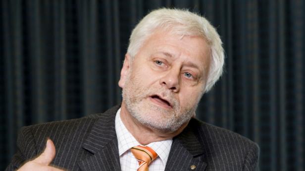 Ein Mann mit grauem Haar und Anzug spricht.