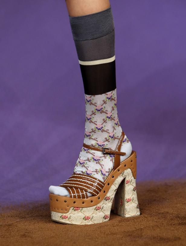 Ein Fuß trägt eine Plateausandale mit floralem Muster und Socken in verschiedenen Designs.