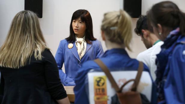 Ein humanoider Roboter in einem blauen Blazer steht inmitten einer Menschenmenge.