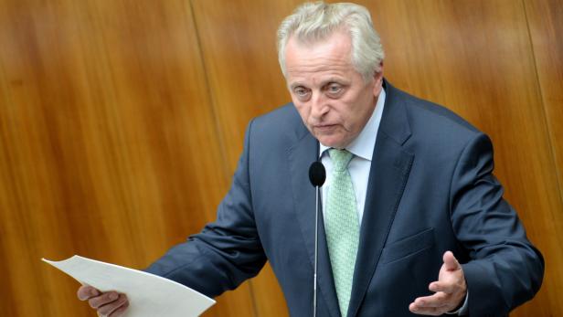 Ein Mann in einem Anzug spricht am Rednerpult und hält ein Blatt Papier.