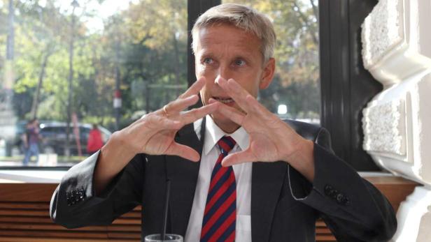 Ein Mann im Anzug gestikuliert vor einem Fenster.