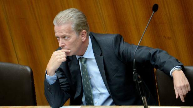 Ein Mann im Anzug sitzt nachdenklich an einem Tisch mit Mikrofon.