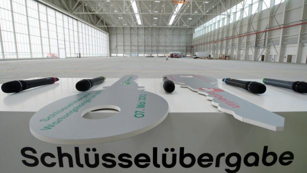 Zwei übergroße Schlüssel und mehrere Mikrofone stehen vor einem leeren Wartungshangar.