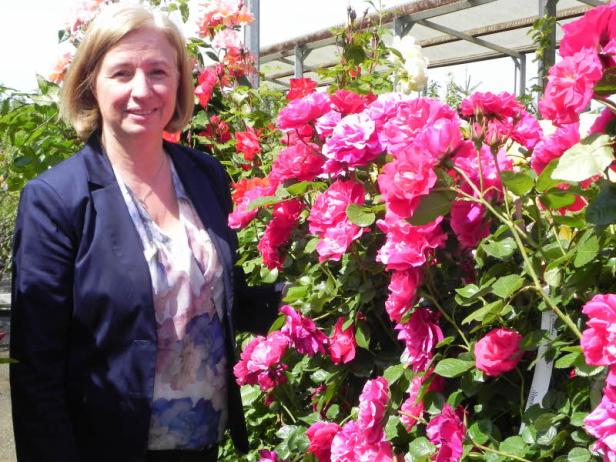 Eine Frau steht vor einem Busch mit rosa Rosen.