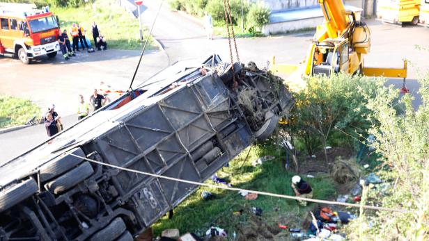 Ein umgestürzter Bus wird von einem Kran angehoben, während Feuerwehrleute und andere Personen zusehen.