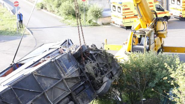 Ein umgestürzter Bus wird von einem Kran angehoben, während im Hintergrund Rettungswagen stehen.