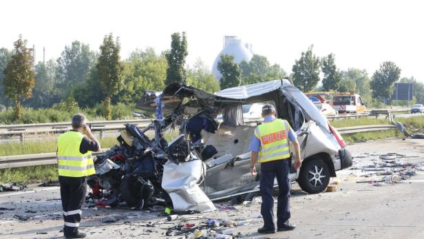 Zwei Polizisten stehen an der Unfallstelle eines völlig zerstörten Kleintransporters.