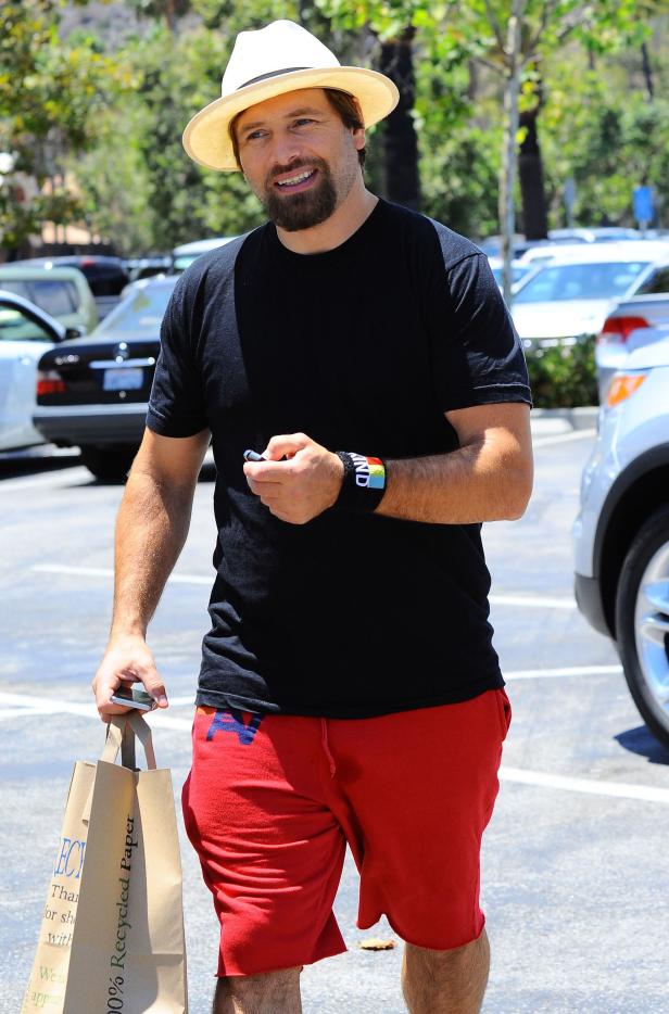 Ein Mann mit Hut, schwarzem T-Shirt und roter Hose trägt eine Einkaufstasche.