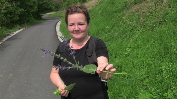 Eine Frau hält eine blühende Pflanze in der Hand, während sie auf einem Weg steht.