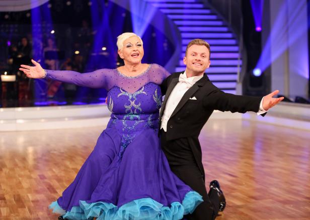 Ein Tanzpaar in festlicher Kleidung posiert auf einer Bühne.