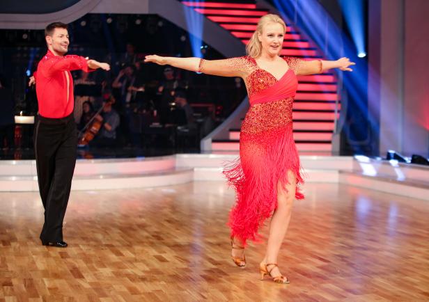 Ein Tanzpaar in roten Kostümen tanzt auf einer Bühne.