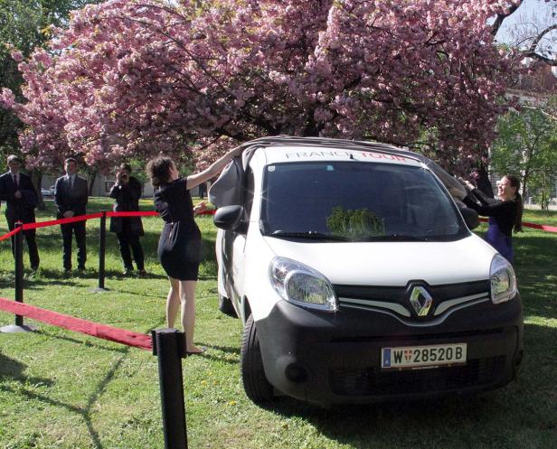 Zwei Frauen enthüllen einen weißen Renault Kangoo mit der Aufschrift „France Tour“ vor einem blühenden Baum.