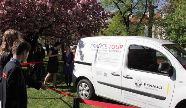 Ein weißer Renault „France Tour“-Wagen steht vor einer Gruppe von Menschen im Park.