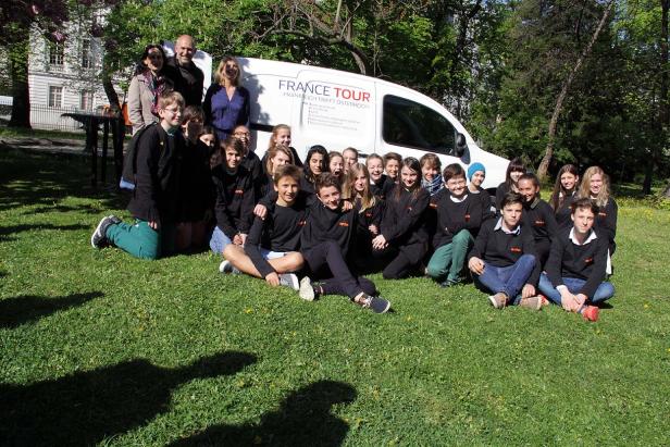 Eine Gruppe von Schülern posiert vor einem „France Tour“-Bus auf einer Wiese.