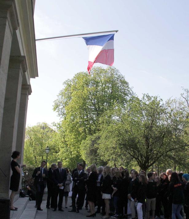 Eine Gruppe von Menschen steht unter der französischen Flagge vor einem Gebäude.