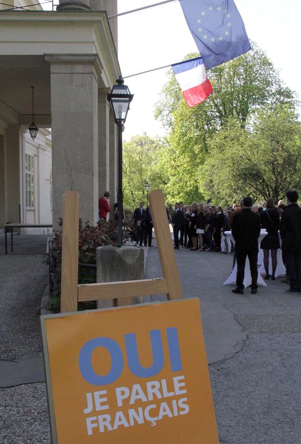 Eine Gruppe von Menschen steht vor einem Gebäude unter der französischen und der EU-Flagge.