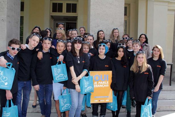Eine Gruppe Jugendlicher mit Sonnenbrillen posiert mit ARTE-Taschen und einem „Je parle français“-Schild.