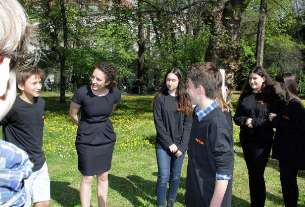 Eine Gruppe von Jugendlichen und eine Frau stehen auf einer Wiese im Park.
