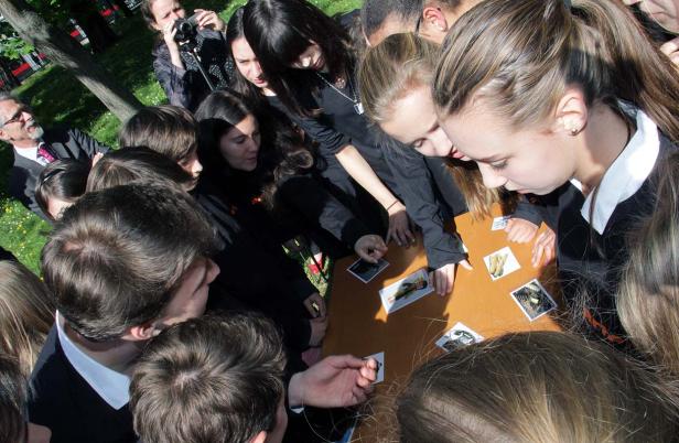 Eine Gruppe von Jugendlichen betrachtet Fotos auf einem Tisch im Freien.