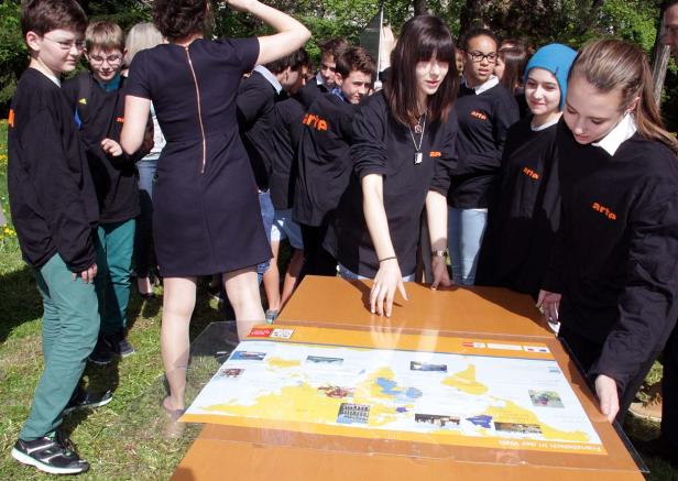 Eine Gruppe von Jugendlichen betrachtet eine Weltkarte auf einem Tisch im Freien.