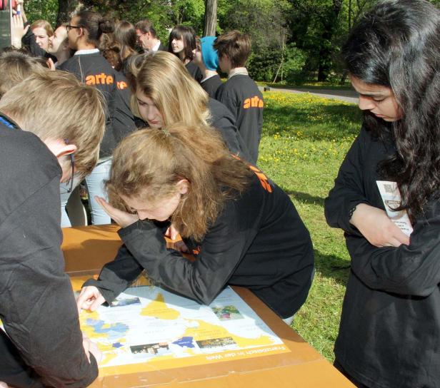 Eine Gruppe Jugendlicher betrachtet eine Weltkarte im Freien.