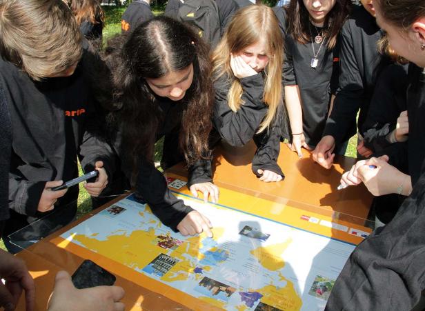 Eine Gruppe von Schülern betrachtet eine Weltkarte auf einem Tisch.