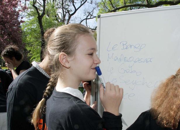 Ein junges Mädchen schreibt mit einem blauen Stift auf ein Whiteboard mit afrikanischen Ortsnamen.