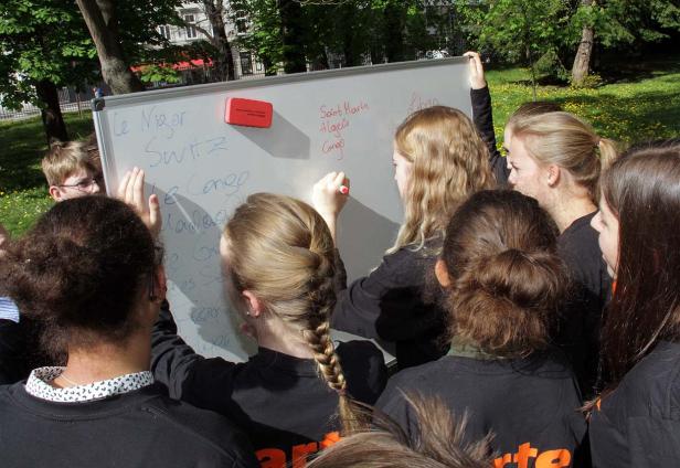 Eine Gruppe von Jugendlichen schreibt Ländernamen auf eine Tafel im Freien.