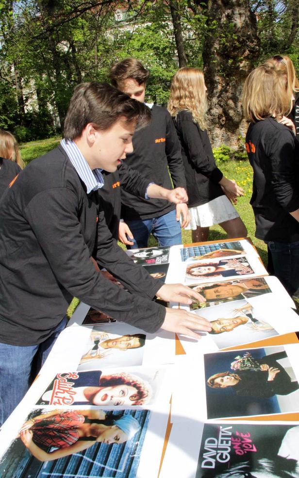 Eine Gruppe junger Leute steht an einem Tisch mit Plattencovern, darunter Edith Piaf und David Guetta.