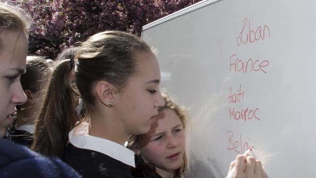 Schülerinnen schreiben Ländernamen wie Libanon, Frankreich und Haiti auf eine Tafel.