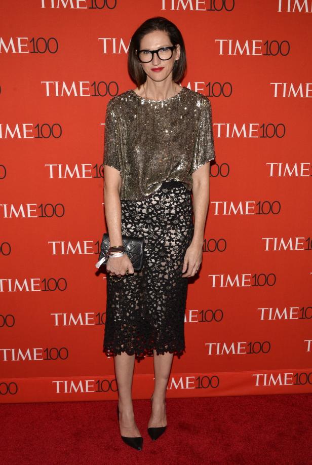 Eine Frau mit Brille, goldenem Oberteil und schwarzem Spitzenrock auf einem roten Teppich mit „TIME100“-Schriftzug.