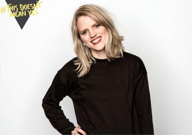 Eine lächelnde Frau mit blonden Haaren und einem schwarzen Pullover posiert vor einem weißen Hintergrund.