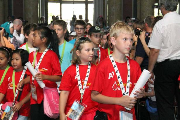 Eine Gruppe Kinder mit roten T-Shirts und A1-Lanyards steht in einem Raum.