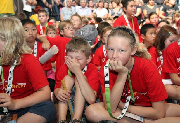 Eine Gruppe von Kindern sitzt auf dem Boden und schaut zu.