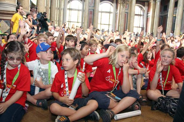 Eine Gruppe Kinder sitzt auf dem Boden und hebt die Hände.
