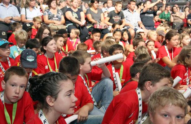 Eine große Gruppe von Kindern und Erwachsenen sitzt auf Tribünen.